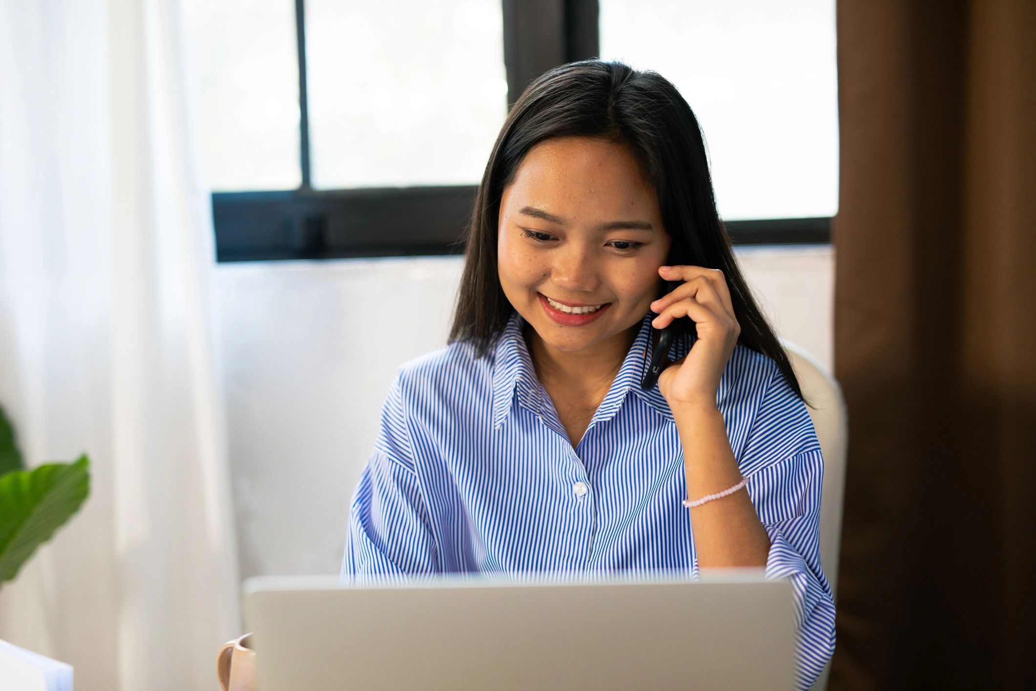 Woman working on laptop while talking on phone